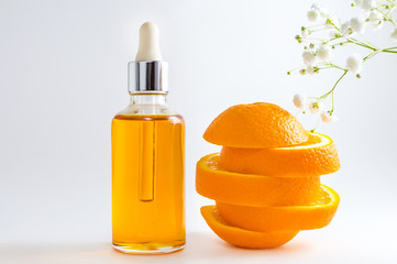 Vitamin C serum in cosmetic bottle with dropper, sliced orange and flowers on white background. Organic SPA cosmetics with herbal ingredients.