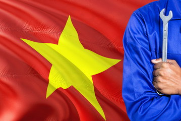 Vietnamese Mechanic in blue uniform is holding wrench against waving Vietnam flag background. Crossed arms technician.