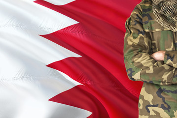 Fototapeta na wymiar Crossed arms Bahraini soldier with national waving flag on background - Bahrain Military theme.