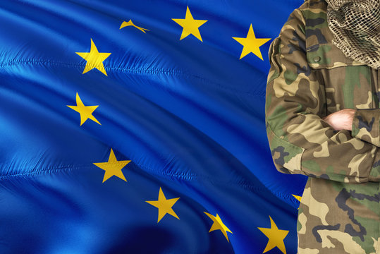 Crossed arms soldier with national waving flag on background - European Union Military theme.