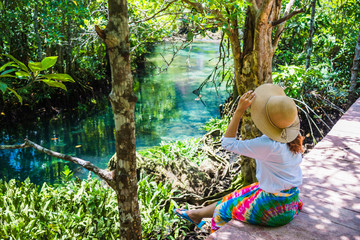 Naklejka na ściany i meble Asian women travel relax, travel nature in the holiday. Nature Study in the forest. women happy enjoying sitting and watching the lake mangrove forest. tha pom-klong-song-nam at krabi. summer
