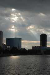 Obraz premium Rays of the sun coming through clouds over the buildings near the river