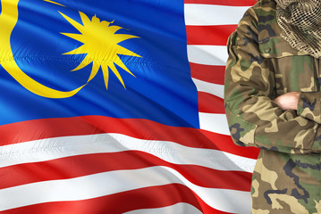 Crossed arms Malaysian soldier with national waving flag on background - Malaysia Military theme.