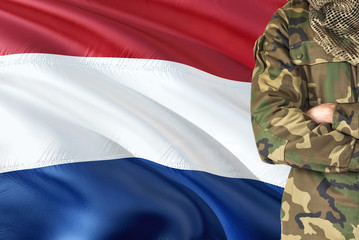 Crossed arms Dutch soldier with national waving flag on background - Netherlands Military theme.