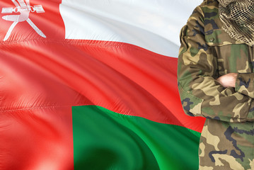 Crossed arms Omani soldier with national waving flag on background - Oman Military theme.