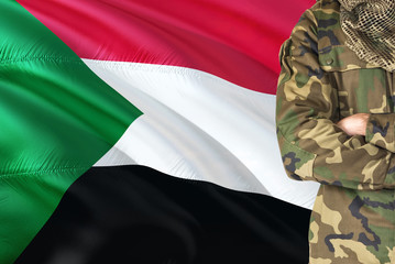 Crossed arms Sudanese soldier with national waving flag on background - Sudan Military theme.