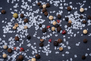 Coarse Sea Salt and Rainbow Peppercorns on natural stone background.