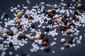 Coarse Sea Salt and Rainbow Peppercorns on natural stone background.