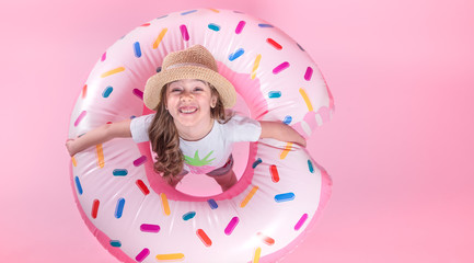 Obraz na płótnie Canvas A little child girl lying on a donut inflatable circle. Pink background. Top view. Summer concept.