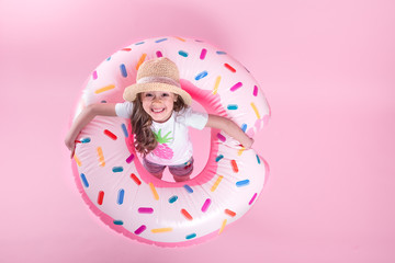 A little child girl lying on a donut inflatable circle. Pink background. Top view. Summer concept.