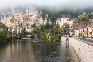 Obraz premium A traditional boat sails along the Dordogne River in front of the Château de la Malartrie at La Roque-Gageac in the Perigord region of France