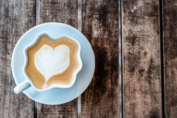 deformed mug of cappuccino coffee with a painted heart stands on a wooden textured table. top view,...