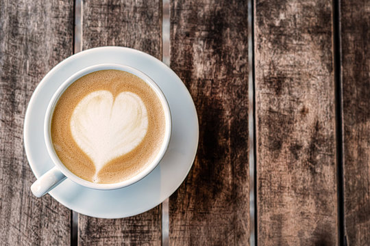 a mug of cappuccino coffee with a painted heart stands on a wooden textured table. top view, close-up. free empty space.