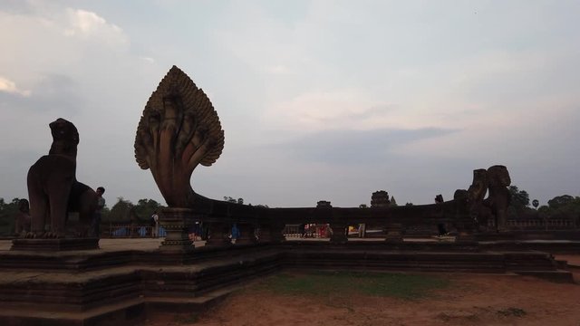 evening view of the temple of Angkor Wat, across the moat, in the foreground a dilapidated stone lion and the figure of a multi-headed snake Naga, in the background visible tourists. Cambodia.