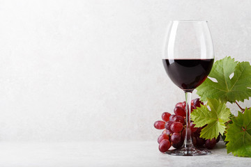 A glass of red wine on the table, grapes and grape leaves. Light background. - obrazy, fototapety, plakaty