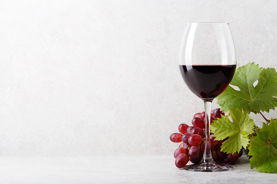 A glass of red wine on the table, grapes and grape leaves. Light background.