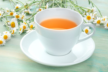 A cup of chamomile tea on a teal blue background with a bouquet of fresh flowers