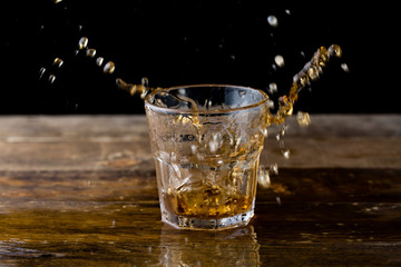 Whiskey splash. Glass of whiskey with ice cubes splashing out.