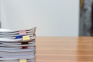 Close up pile of unfinished paperwork on office desk waiting to be managed and inspected. Stack of homework assignment with colorful paper clips. Report papers stacks. Business and education concept.