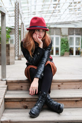 Sensual woman in a red bowler hat with long hair sitting on wooden stairs.