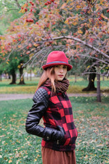 Sensual woman in a red bowler hat with long hair walking in park. Autumn fashion.