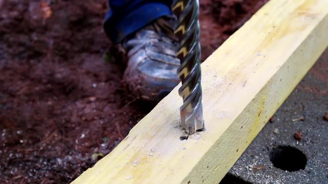 Closeup of industry worker drilling a wood rafter with a big drill. Manual making of a foundation with concrete, cinderblock and wood.