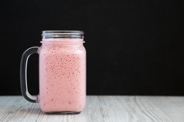 Mason glass jar mug filled with strawberry banana smoothie, side view. Copy space.