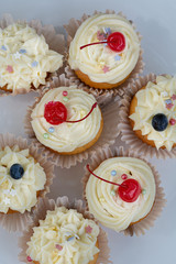 Homemade Cupcakes-muffins with cream cheese frosting, decorated with cherry and fresh blueberries. Top view flat lay white background.Selective focus