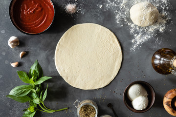 Top view of raw dough, ingredients and spices for pizza Margherita with tomato sauce and Mozzarella...