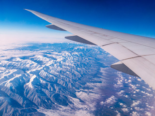 Obraz premium Aerial view of Taurus Mountains covered with snow. Airplane wing while flying seen through window of passenger aircraft. Flying at 35000 feet over ground.