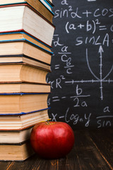 Books and an apple on a wooden table, against the background of a chalkboard with formulas. Teacher's day concept and back to school.