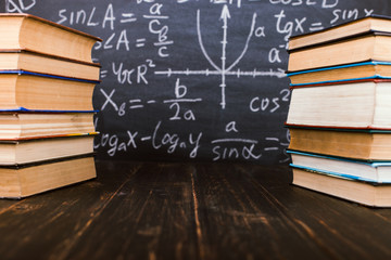 Books on a wooden table, against the background of a chalk board with formulas. Teacher's day concept and back to school.