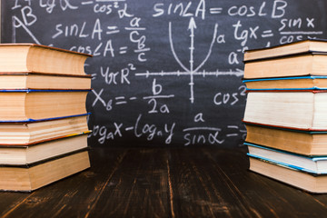 Books on a wooden table, against the background of a chalk board with formulas. Teacher's day concept and back to school.