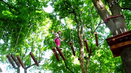 Happy little girl in summer. Hike and kids concept. Beautiful Little girl climbing and having fun in adventure Park. Carefree childhood.