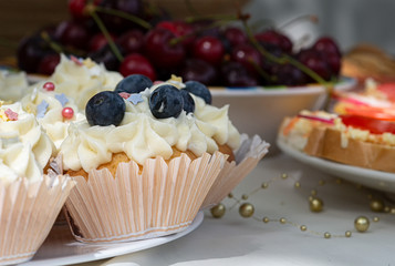 Homemade Cupcakes-muffins with cream cheese frosting, decorated with cherry and fresh blueberries. Selective focus