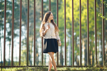 Vape teenager. Young cute girl in casual clothes smokes an electronic cigarette in front of a metal...