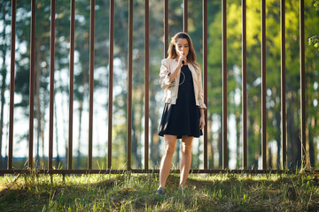 Vape teenager. Young cute girl in casual clothes smokes an electronic cigarette in front of a metal...