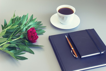 Peony flower with black notebooks, cup of coffee and a pen