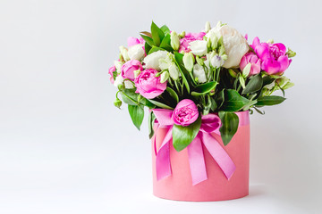 Obraz na płótnie Canvas Arrangement of flowers in a hat box. Bouquet of pink and white peonies, eustoma, spray rose in a pink box with an oasis on a white background with copy space