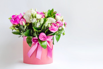 Arrangement of flowers in a hat box. Bouquet of pink and white peonies, eustoma, spray rose in a pink box with an oasis on a white background with copy space