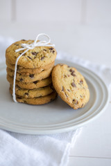 Close-up of nut and chocolate chips cookies on a white plate and linen with bright colors and coffee walnuts and spoon in soft-focus in the background