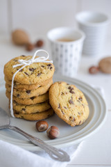 Close-up of nut and chocolate chips cookies on a white plate and linen with bright colors and coffee walnuts and spoon in soft-focus in the background