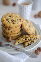 Close-up of nut and chocolate chips cookies on a white plate and linen with bright colors and coffee walnuts and spoon in soft-focus in the background