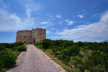 Fototapeta na wymiar Arza fortress on a bright sunny day, a stony road leading to the fortress, green bushes near the road.