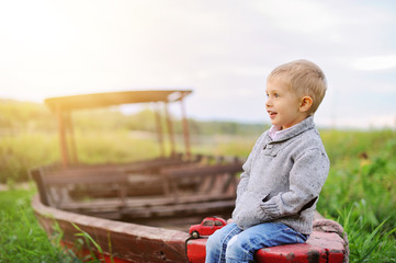 Fototapeta premium Little boy is sitting on the boat. He dreaming of sailing.