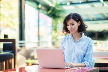 young and beautiful girl with notebook and laptop sitting in a cafe