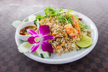 Fried rice with shrimp on the white ceramic dish decorated with orchid and hot spicy dipping sauce put on leather floor the grid pattern. Top view