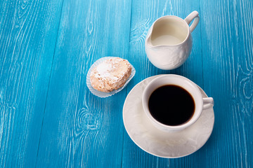 A cup of coffee, milk and a biscuit on a blue wooden table