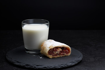 Slice of classic strudel and a glass of milk on a dark background