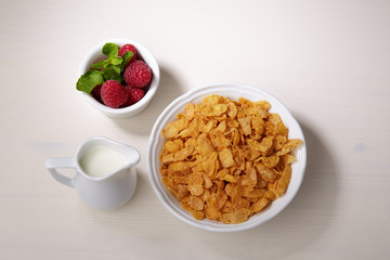 Breakfast set: сornflakes, milk and raspberry with mint leaves on a light wooden background